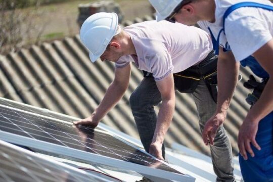 two people installing a solar panel on a roof